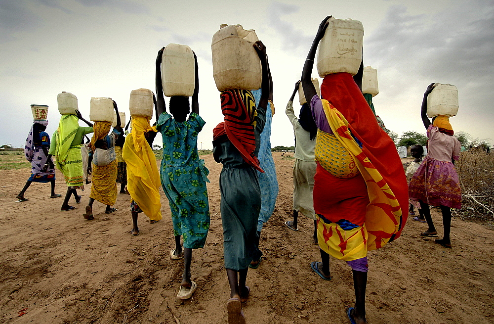 Women carrying water collected from taps installed by international aid agencies in a camp for internally displaced persons (IDPs). They fled their homes after being attacked by Janjaweed militias.