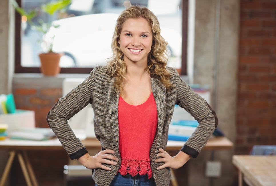 Portrait of confident businesswoman with hands on hip standing in bright office